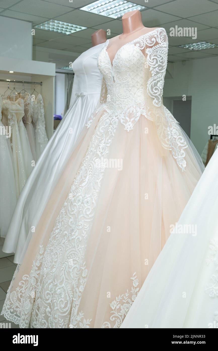 A beautiful cream wedding dress on a mannequin. A wedding dress on the background of other wedding dresses in a wedding salon Stock Photo