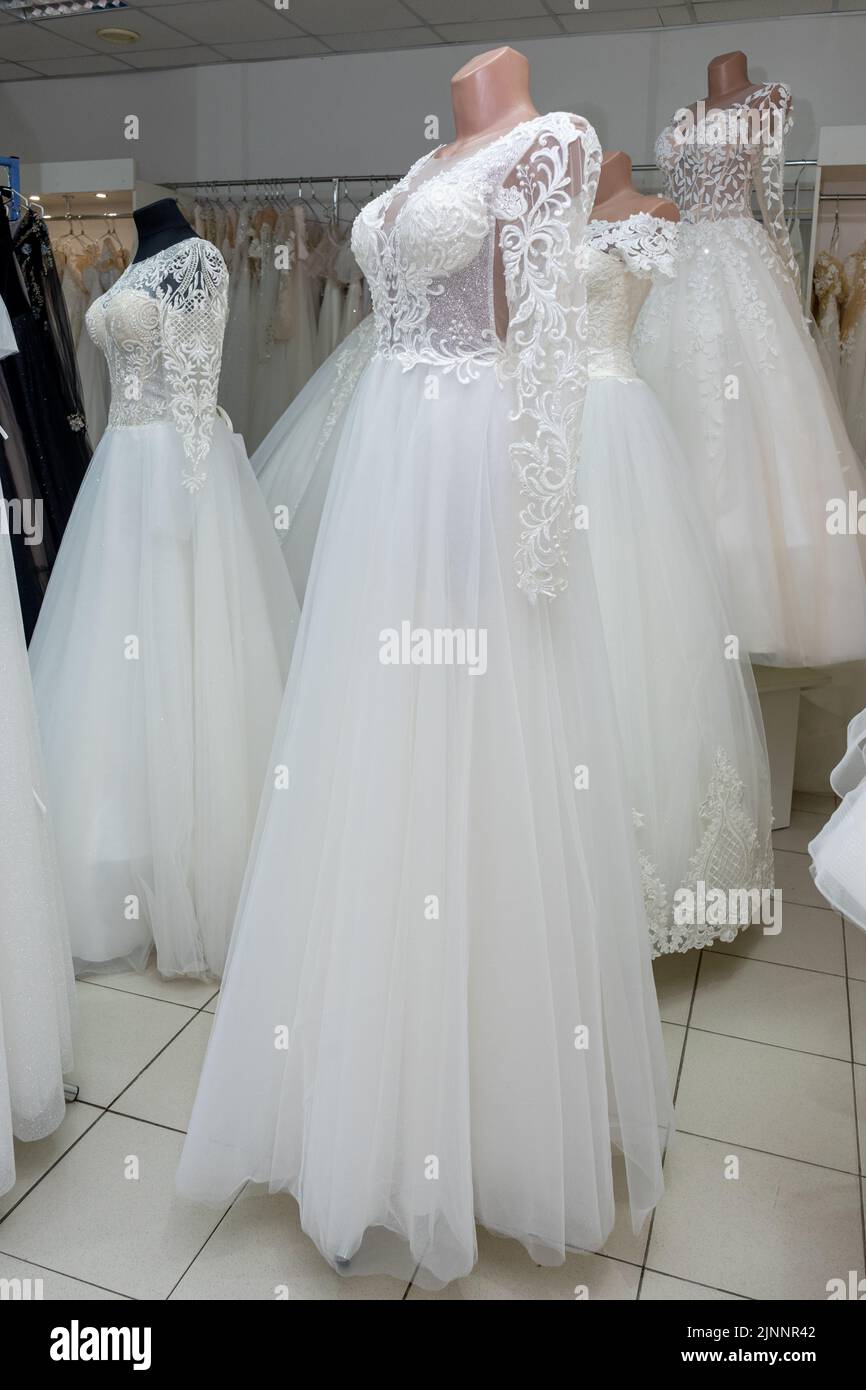 A beautiful white wedding dress on a mannequin. A close-up of a dress against other wedding dresses in a bridal shop Stock Photo
