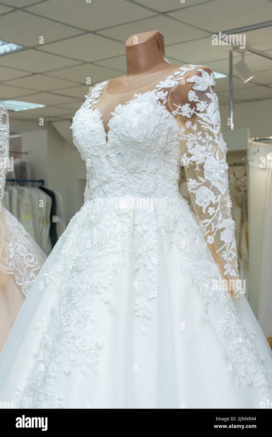 A beautiful white wedding dress on a mannequin. A close-up of a dress against other wedding dresses in a bridal shop Stock Photo