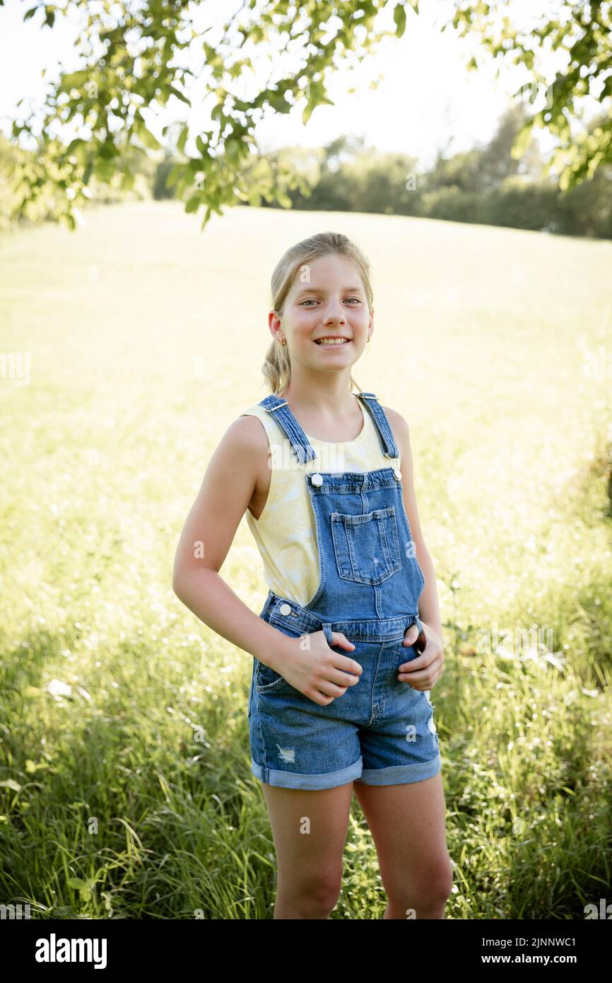 pretty blonde young girl posing with blue dungarees outside in nature and is happy Stock Photo