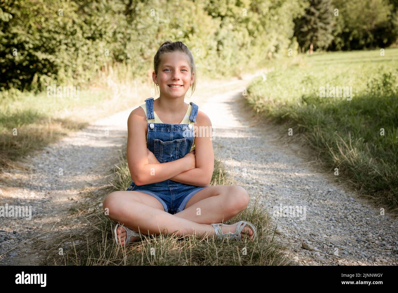 pretty blonde young girl posing with blue dungarees outside in nature ...