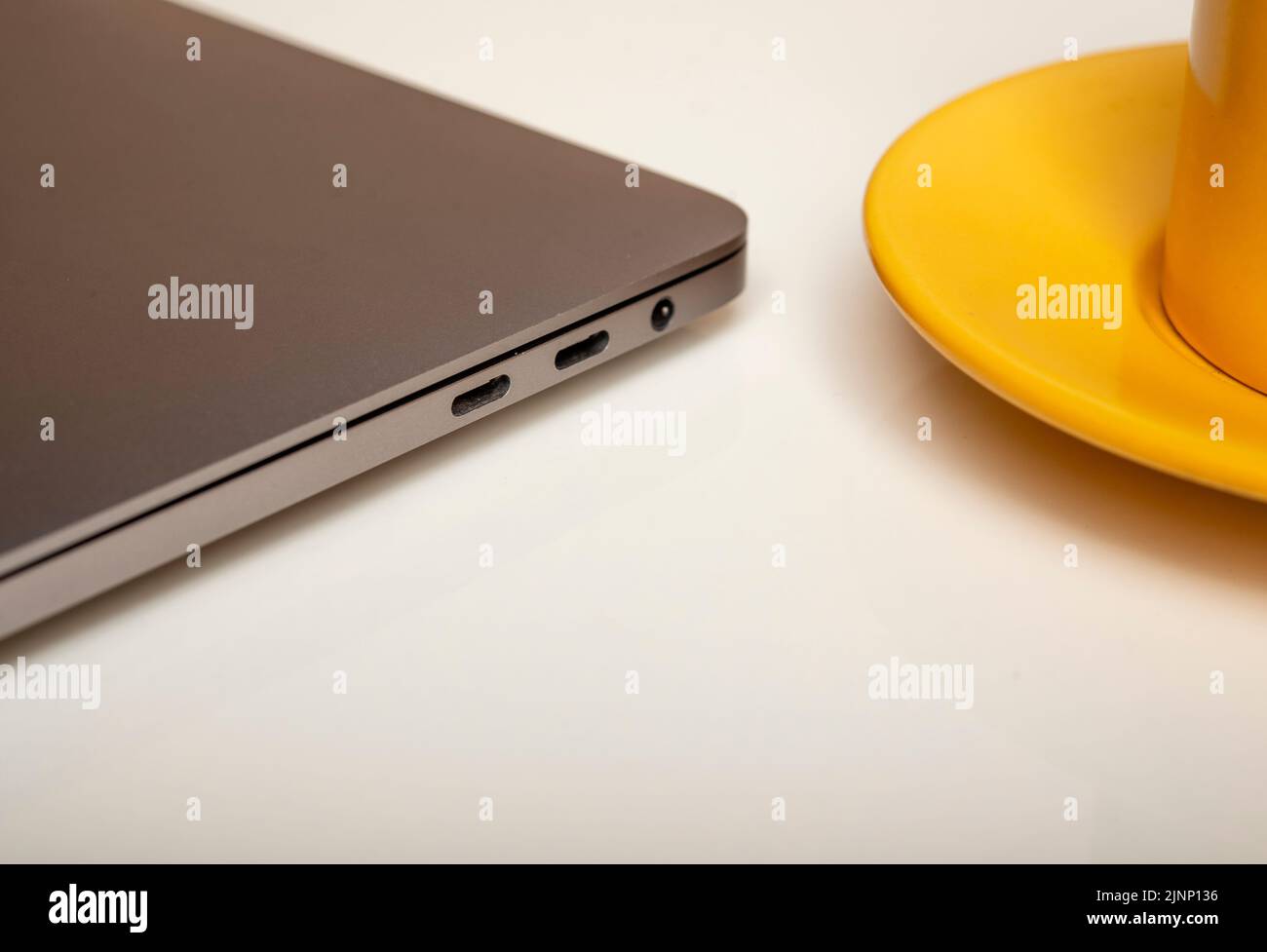 Closeup view of laptop side with yellow coffee cup on white background. Stock Photo