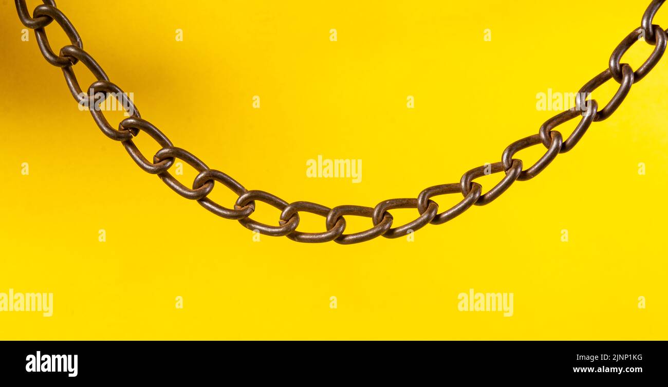 Silver metal chain hanging on yellow background. Stock Photo
