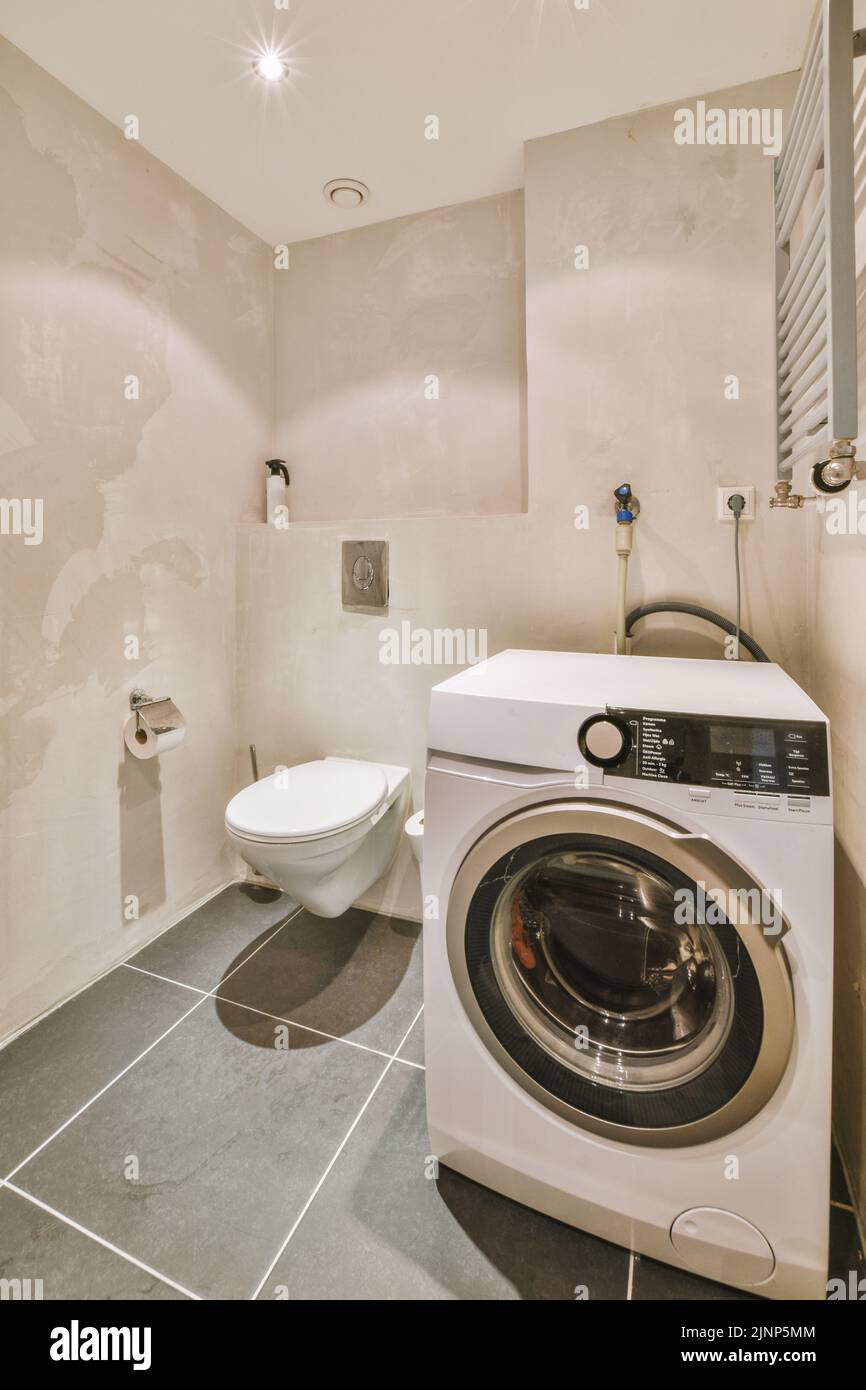 Interior of narrow restroom with washing machine and wall hung toilet ...