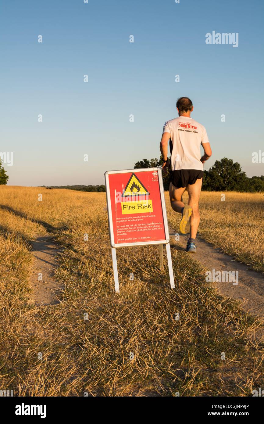 London, England, UK. 12 August 2022.  A jogger running past a Fire Risk sign during a drought in a parched Richmond Park. © Benjamin John Stock Photo