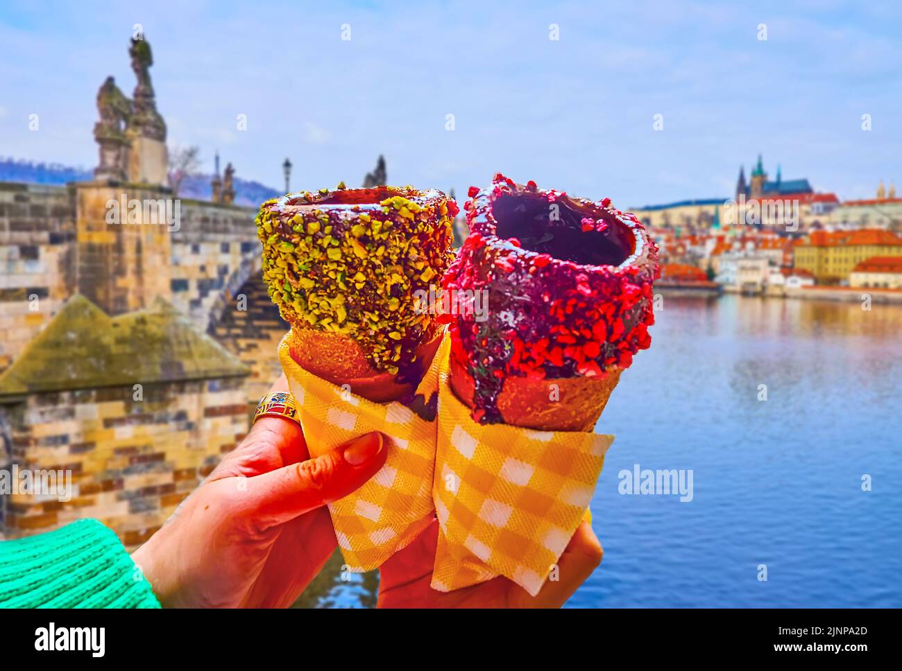 Traditional Czech trdelnik spit cake, covered with chocolate and dry berries in front of Vltava River and stone sculptured Charles Bridge, Prague, Cze Stock Photo