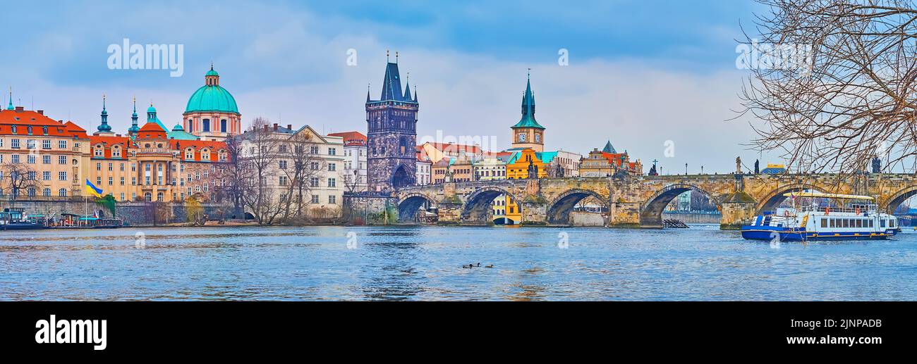 The tourist ferry floats on Vltava River against the Gothic Charles Bridge with Old Town Bridge Tower against the housing of Stare Mesto, Prague, Czec Stock Photo