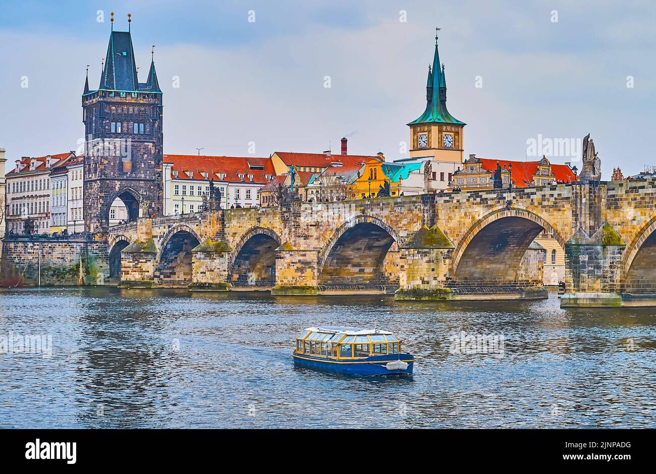 The cityscape of Prague with a boat on Vltava River, Charles Bridge with Gothic Old Town Bridge Tower and Old Town Water Tower with clock in backgroun Stock Photo