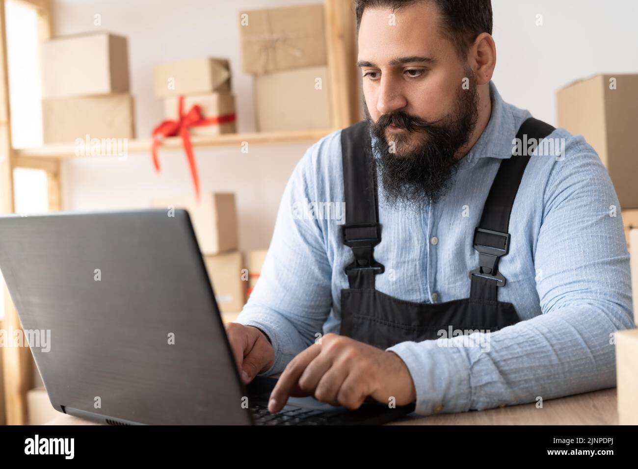 Small business aspiring entrepreneur, small and medium business freelance worker working in a home office man in overalls sits at a table and accepts Stock Photo