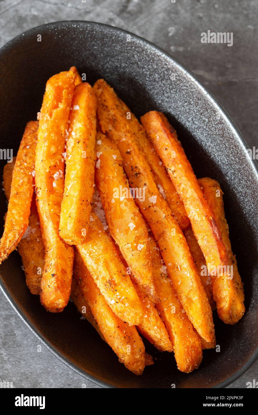 Sweet potato fries, seasoned with sea salt, in a black dish bowl. On a dark stone background Stock Photo