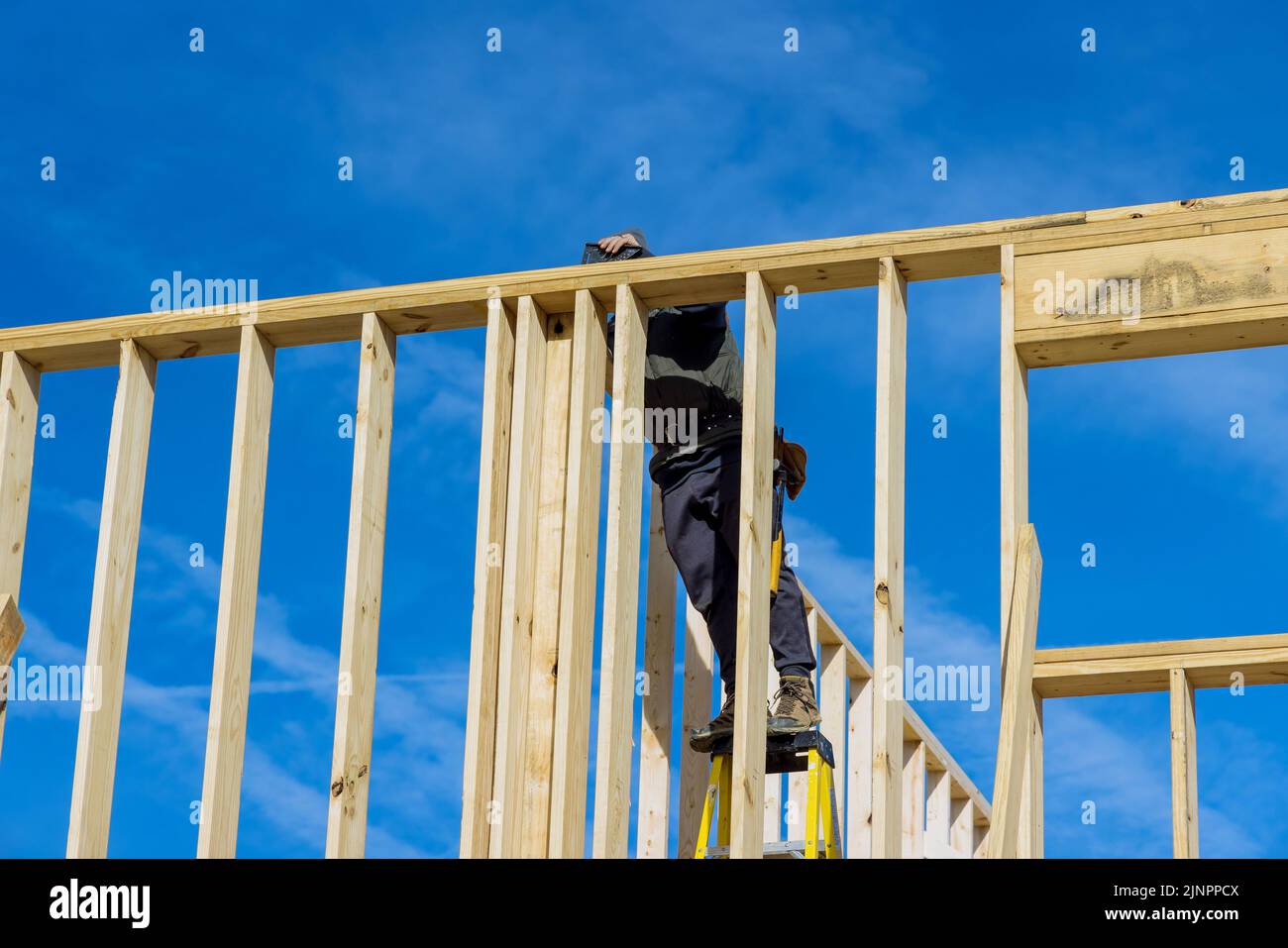 Using an air hammer, a builder nails wooden beams to the wall as part ...