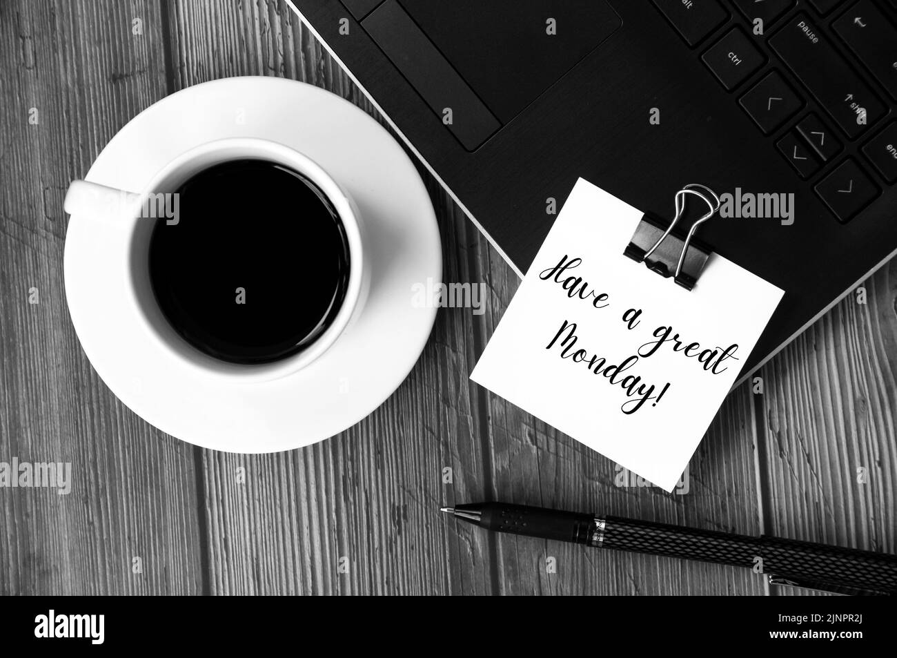 Have a great Monday text on white notepad with laptop, coffee cup and pen in black and white background. Greetings concept Stock Photo