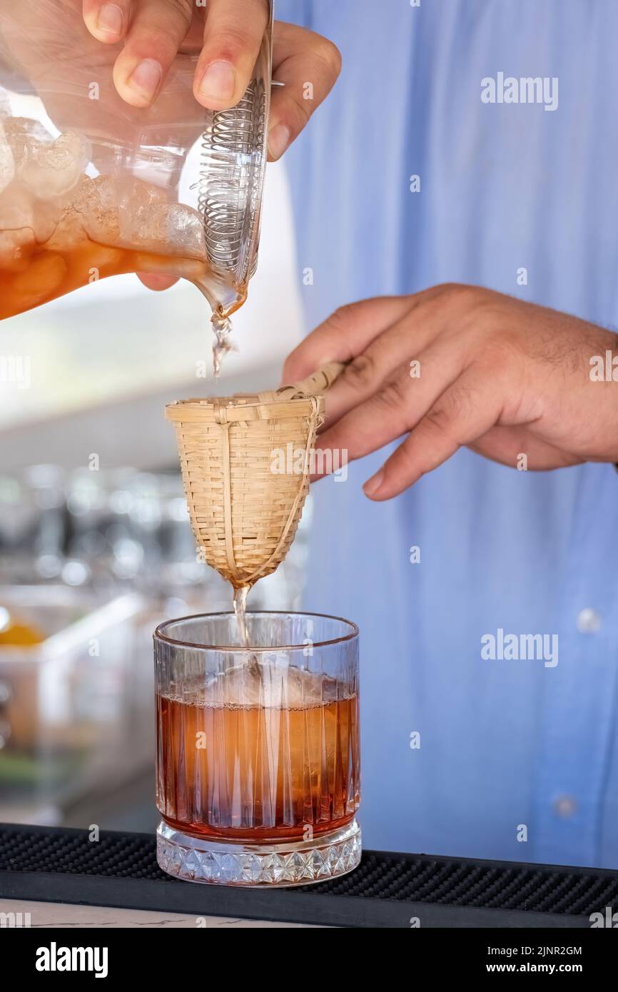 Professional bartender pouring cocktail into glass glass with shaker