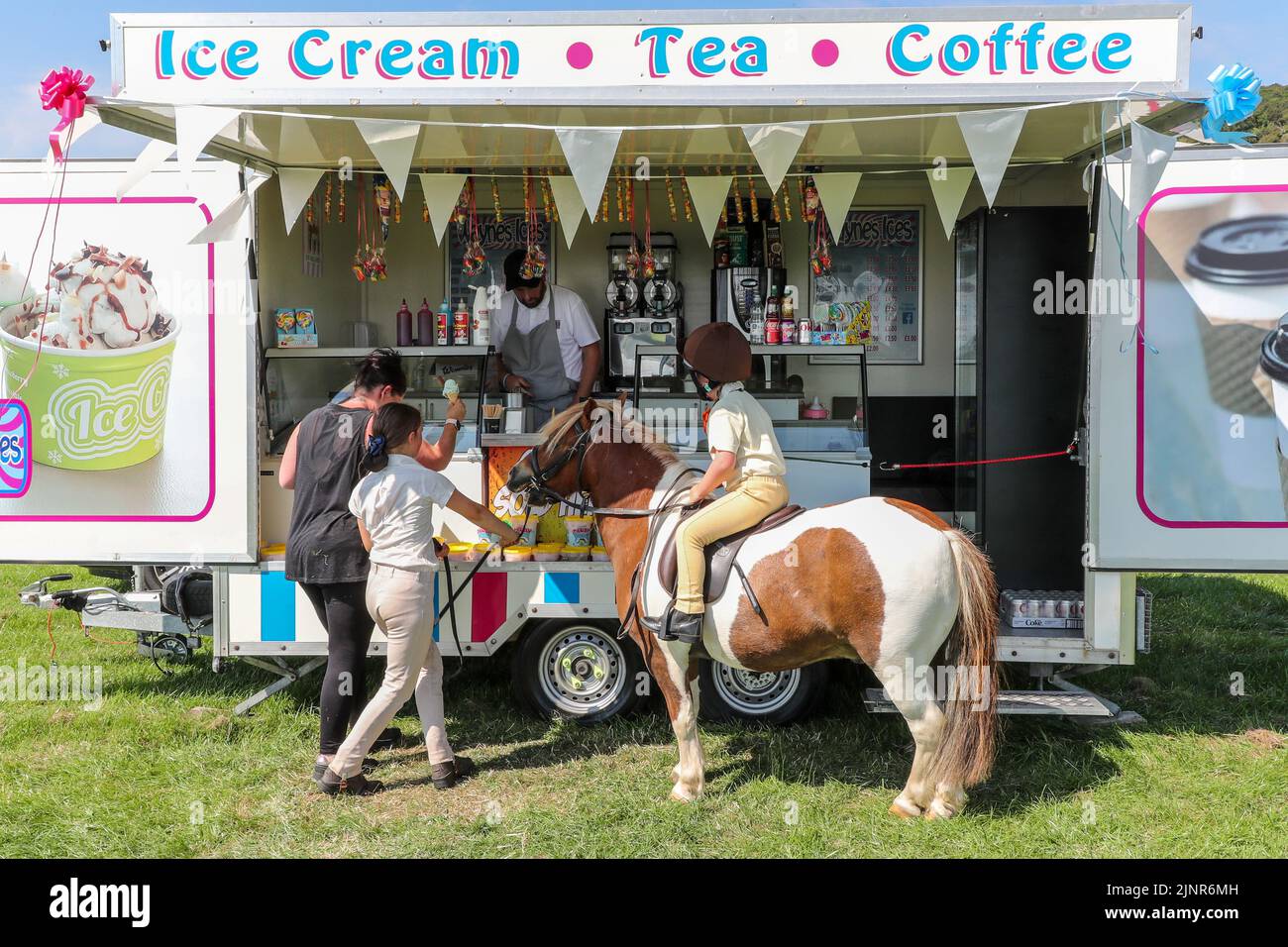 13 August 2022, Craigie, UK. After a tiring and thirsty apprearance at Craigie Country Fair, Micheal, a 12 year old Shetland Pony and his rider Jessica Edgar, aged 5,are rewarded with an ice cream to cool down. Michael's owner Alba Morgan, aged 9, is offering the ice cream to Michael. (Stephanie Edgar, mother is present). Credit: Findlay/ Alamy Live News. Stock Photo