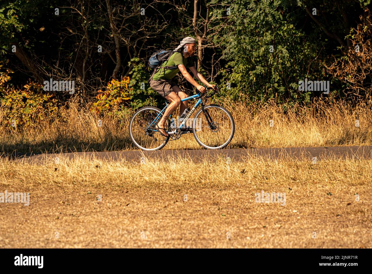 A cyclist passes parched grass in Eastville Park, Bristol. The Met Office has issued an amber warning for extreme heat covering four days from Thursday to Sunday for parts of England and Wales. Picture date: Saturday August 13, 2022. Stock Photo