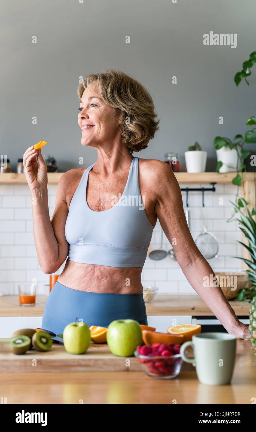Beautiful mature senior woman at home, domestic life and leisure moments - 50-60 years old pretty female adult wearing sportswear eating healthy food Stock Photo