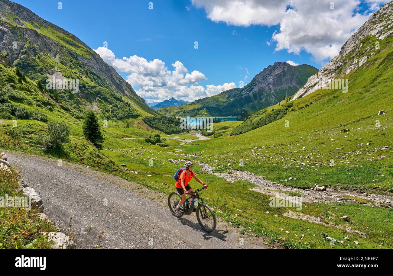 active senior woman, riding her electric mountain bike at Spuller Lake in the Arlberg area near the famous village of Lech, Tirol, Austrian Alps Stock Photo