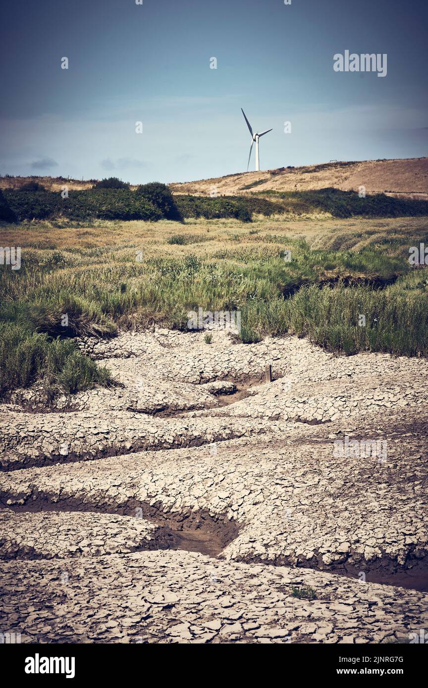 Dried up water channel with solitary wind turbine in background Stock Photo