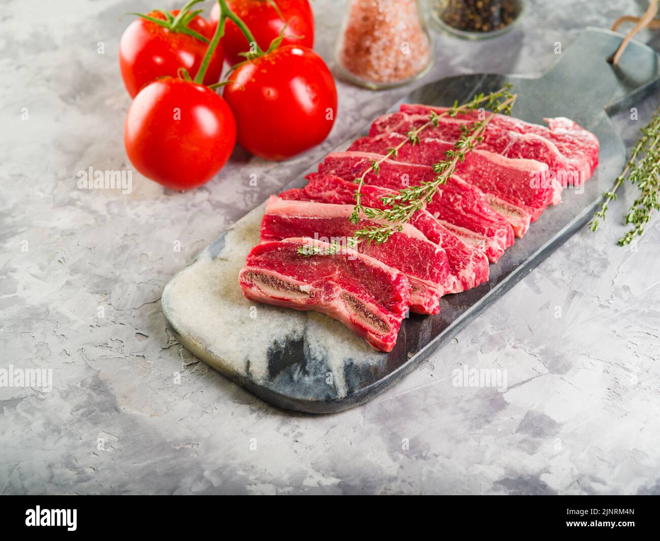 On a light background, fresh meat steaks prepared for cooking, fresh tomatoes, spices, seasonings. Meat recipes. Restaurant and home cooking. Culinary Stock Photo