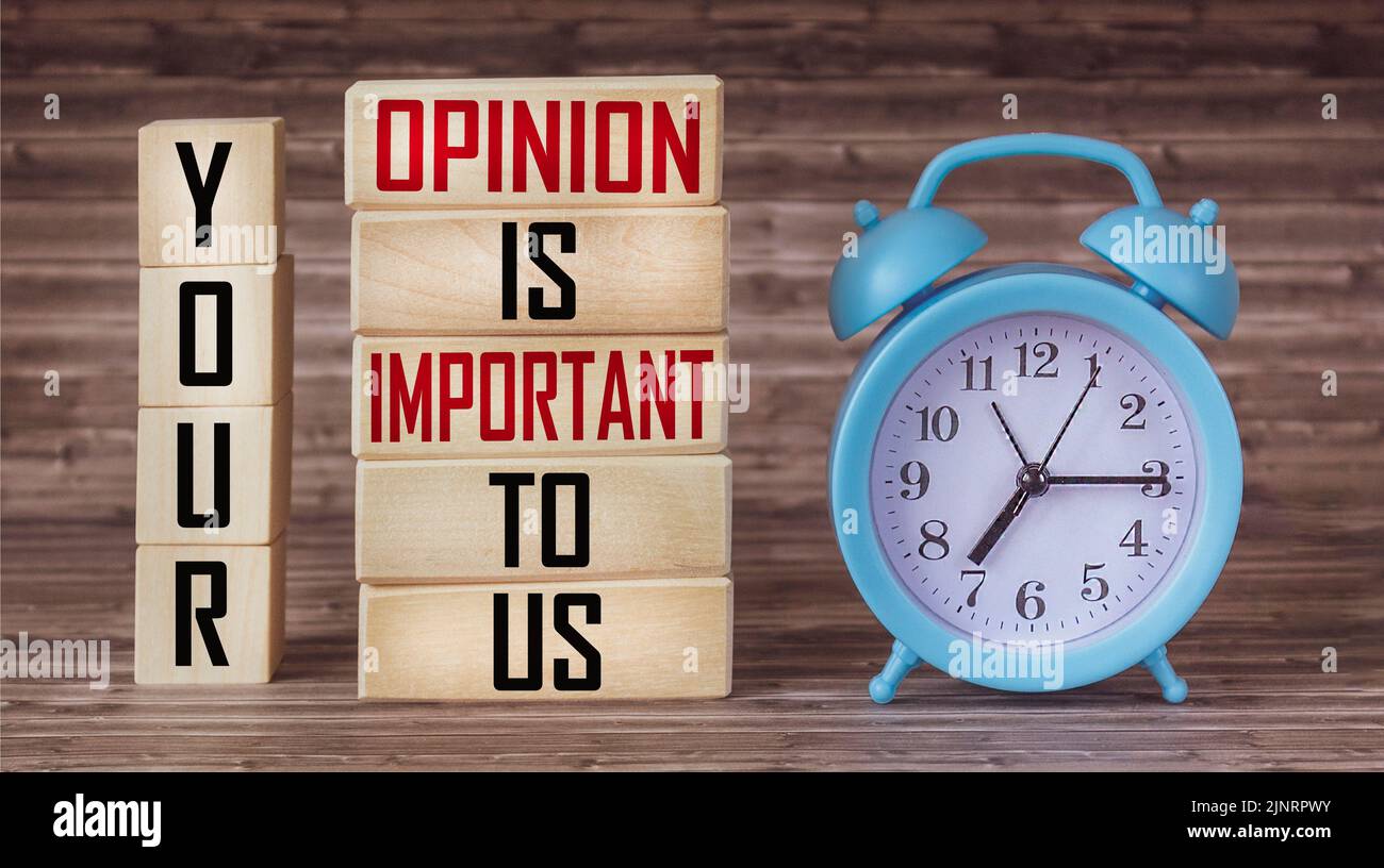 Phrase Your opinion is important to us written on wooden blocks and wooden table with clock Stock Photo