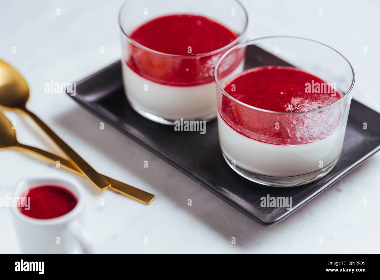 Panna cotta dessert with sauce from berries. Cherries, raspberries and blueberry as decoration. Served in two glasses on bright white background. Trad Stock Photo