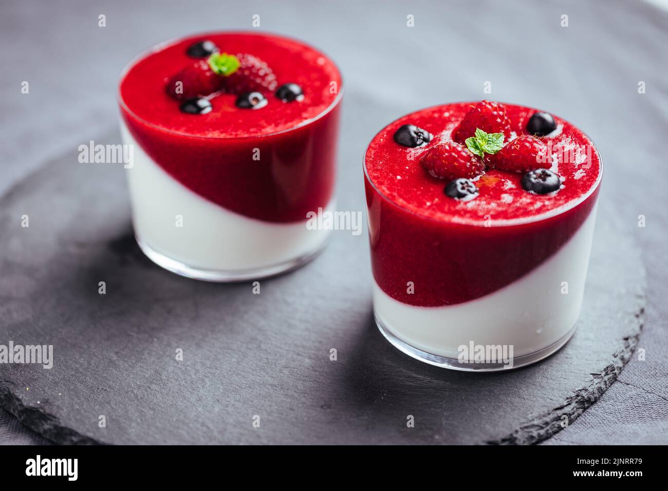 Panna cotta dessert with sauce from berries. Cherries, raspberries and blueberry as decoration. Served in two glasses on bright white background. Trad Stock Photo