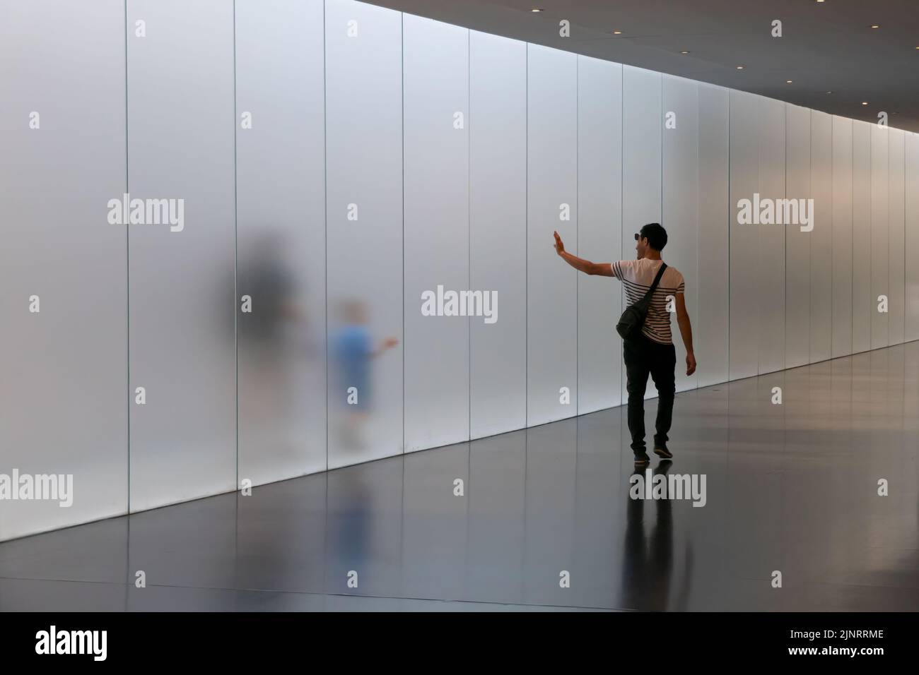 A man waves his hand to say hello as a woman walks with her child behind a transparent walkway in Israel Museum in West Jerusalem Israel Stock Photo