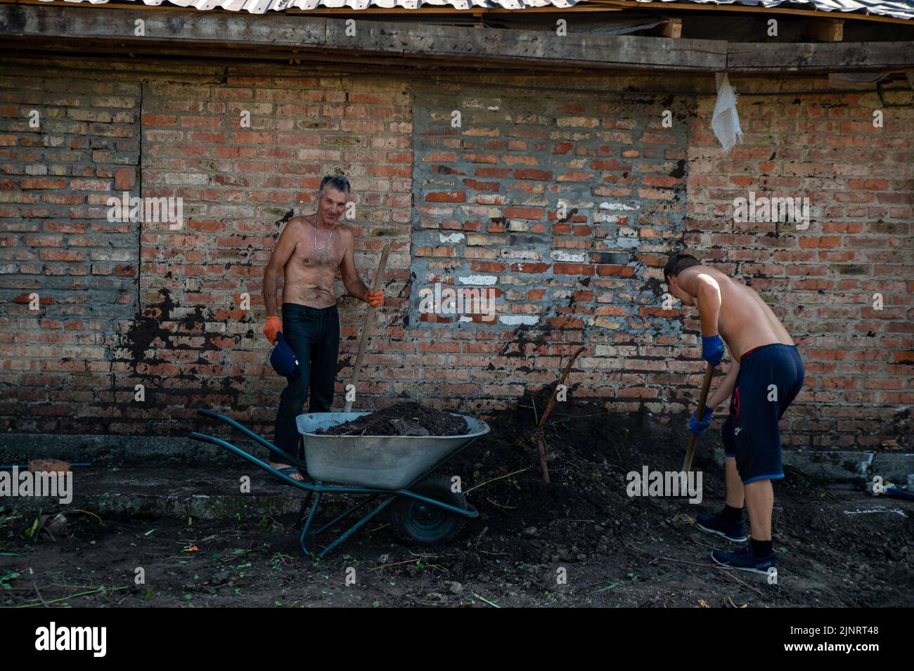 Two men fill in the crater outside the home, cause by shelling in Kushuhum. Outside Zaporizhzhia, the small village finds itself in the crossfire between the Russians and Ukrainians. Stock Photo
