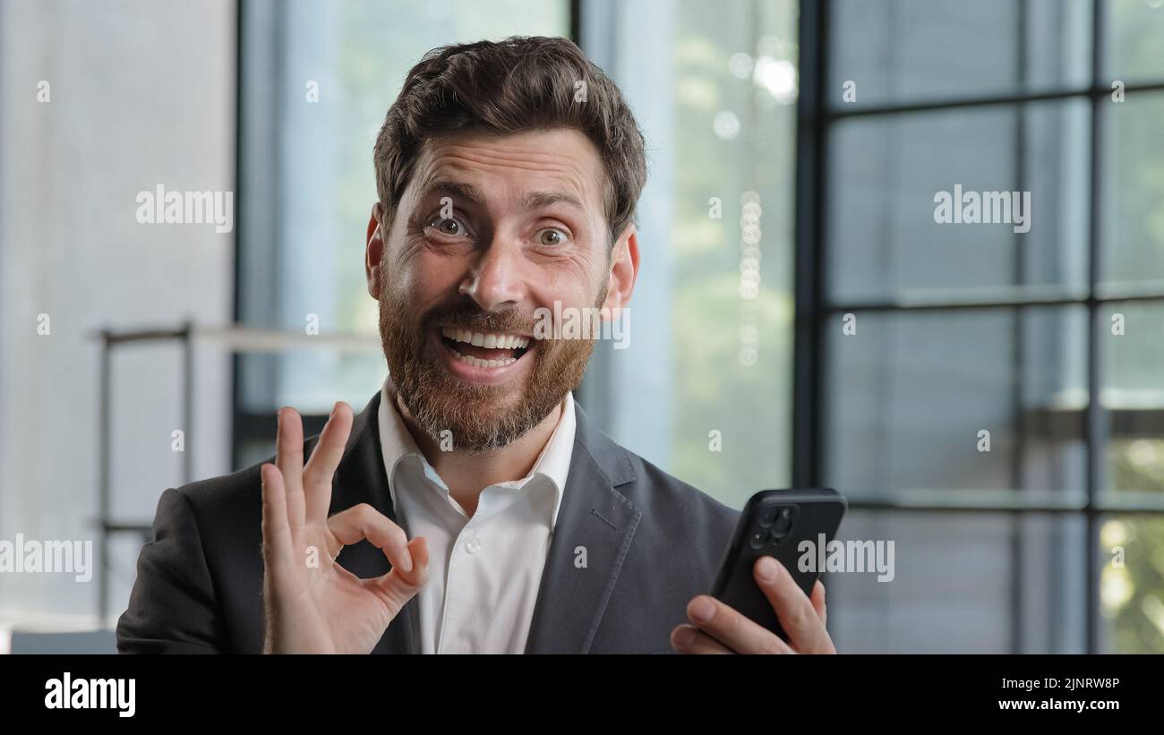 Caucasian bearded businessman 40s boss leader in office with mobile phone victory triumph win victory luck success receive offer money prize Stock Photo