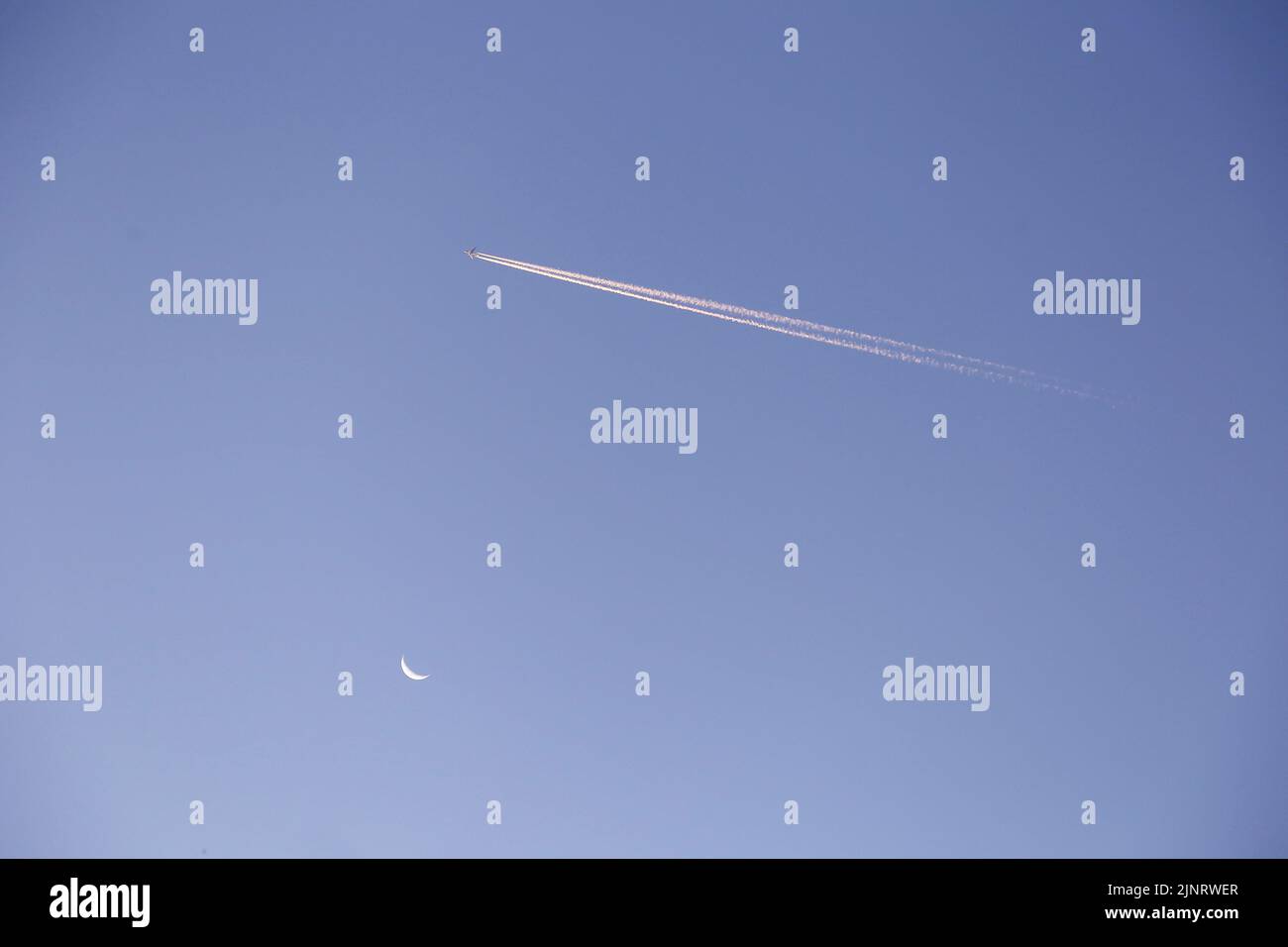 plane moving in the sky, emitting white smoke and moon in the sky Stock Photo