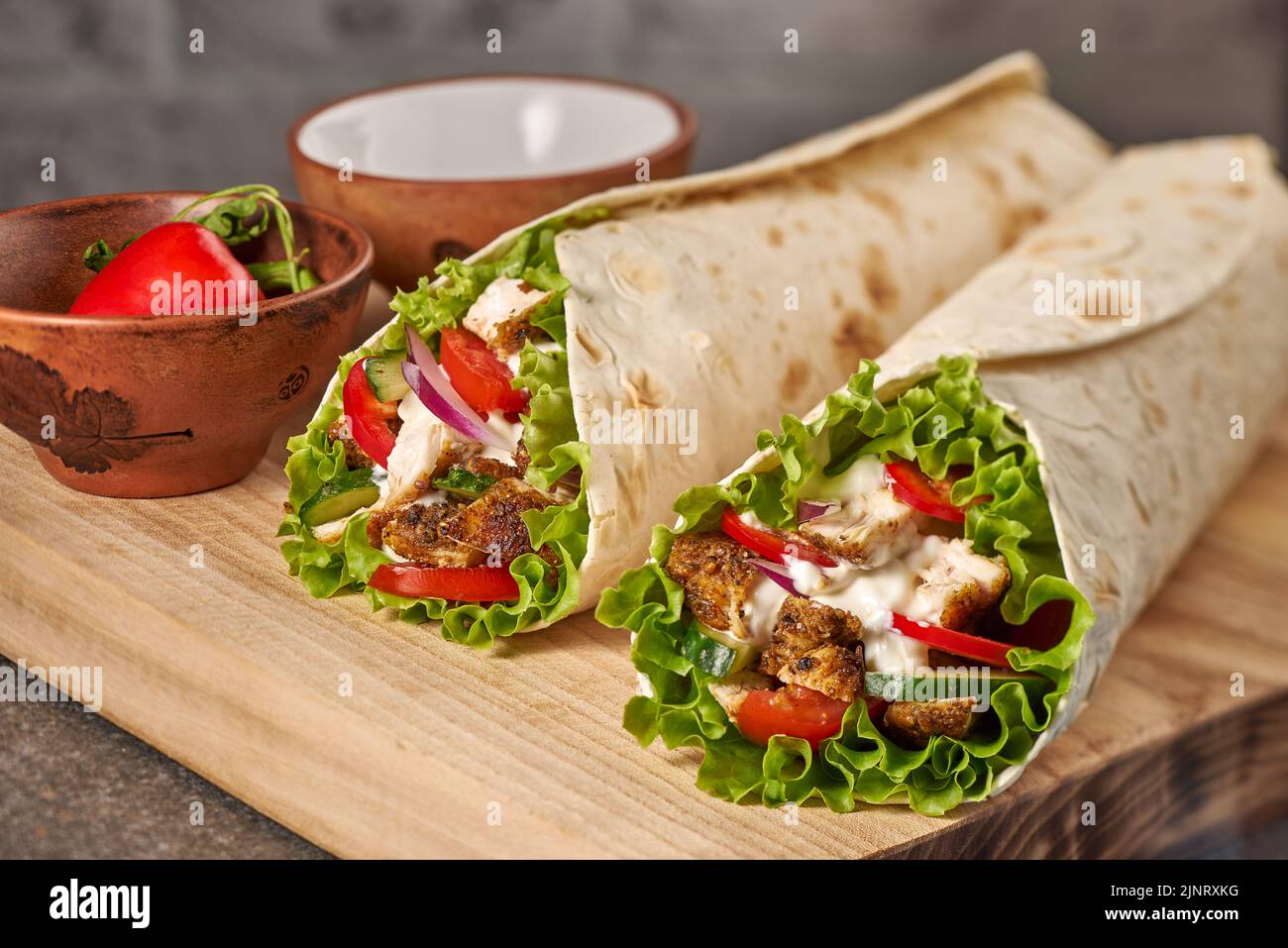 Two chicken wraps on wooden cutting board Stock Photo