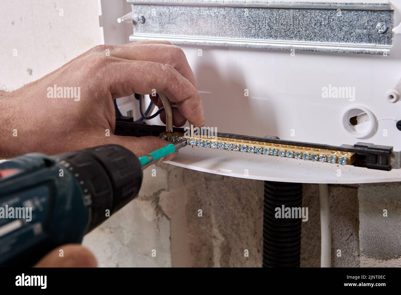 An electrician fixes ends of wires in brass distribution bar using an electric screwdriver. Stock Photo