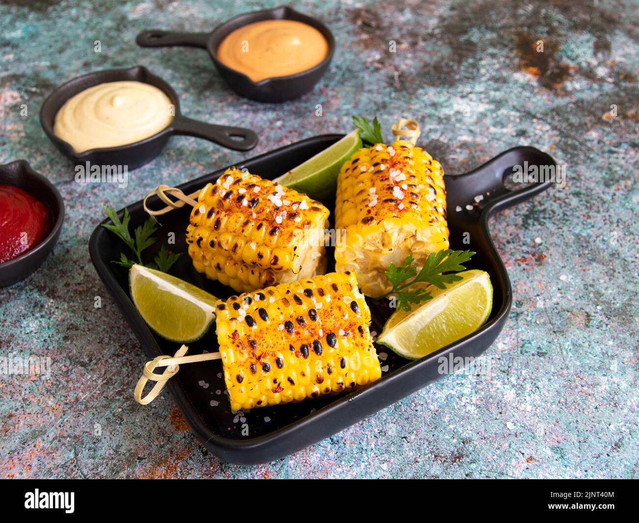 grilled yellow corn with spices lime with white red orange sauce portion Stock Photo