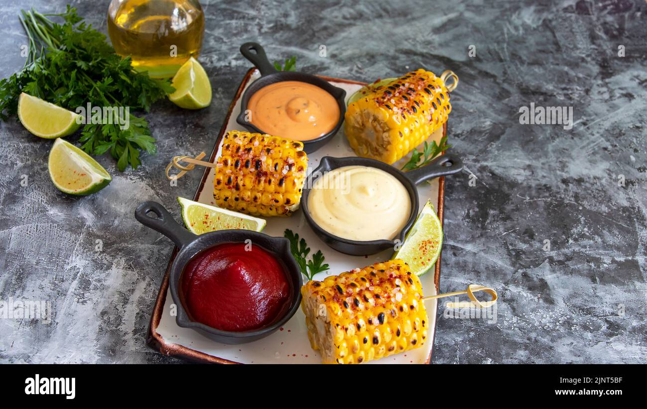 grilled yellow corn with spices lime with white red orange sauce portion close up Stock Photo