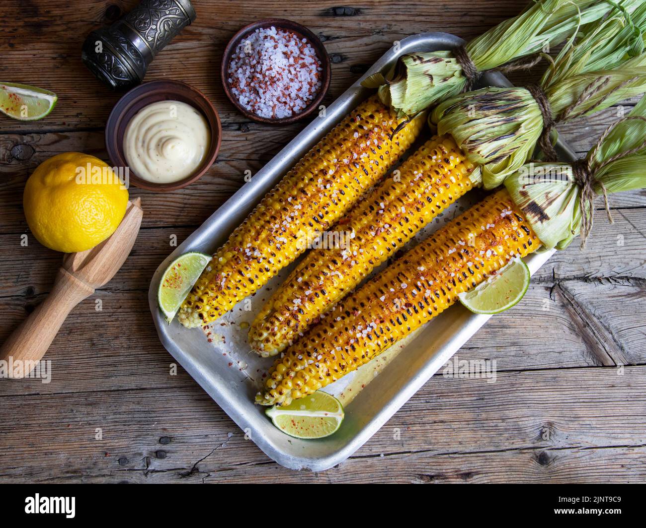 three heads of yellow corn grilled lemon lime spicy white sauce rustic style Stock Photo