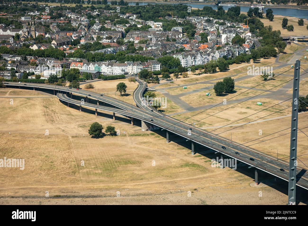 Düsseldorf, NRW, Germany, 13th Aug 2022. Unusually, much of the Rheinkniebrücke and its approach roads in the suburb of Oberkassel stand on dry, parched land at the moment. The River Rhine, one of the busiest inland waterways in the world, has been strongly affected by the ongoing drought and resulting low water levels, caused by prolonged heat of up to 40 degrees and very little rain in the last few weeks. The shipping lane has narrowed down considerably, slowing down traffic, most vessels have also had to considerably reduce their freight weight, leading to supply issues and higher shipping Stock Photo