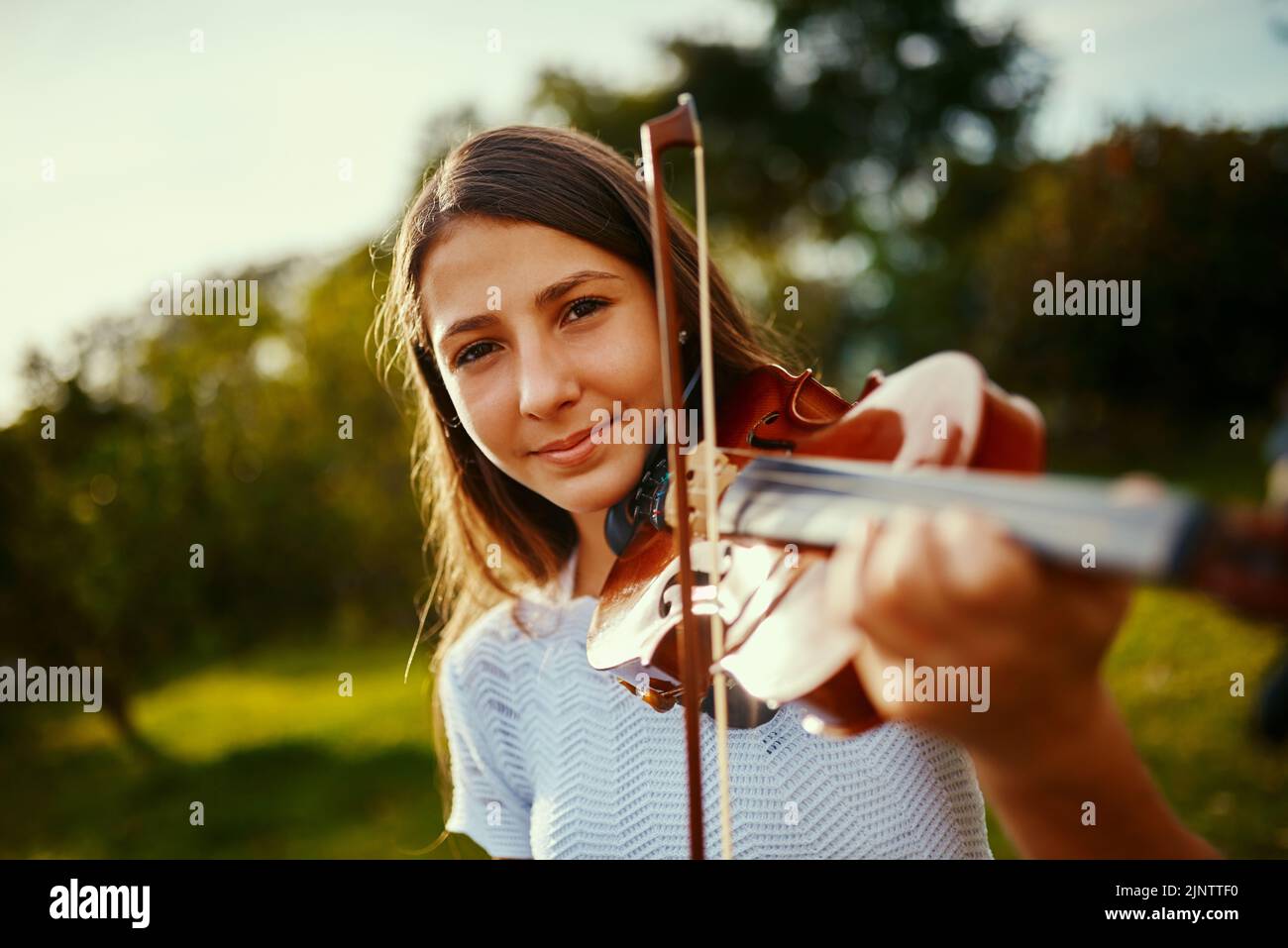 She found her passion at a young age. a young girl playing a violin outdoors. Stock Photo