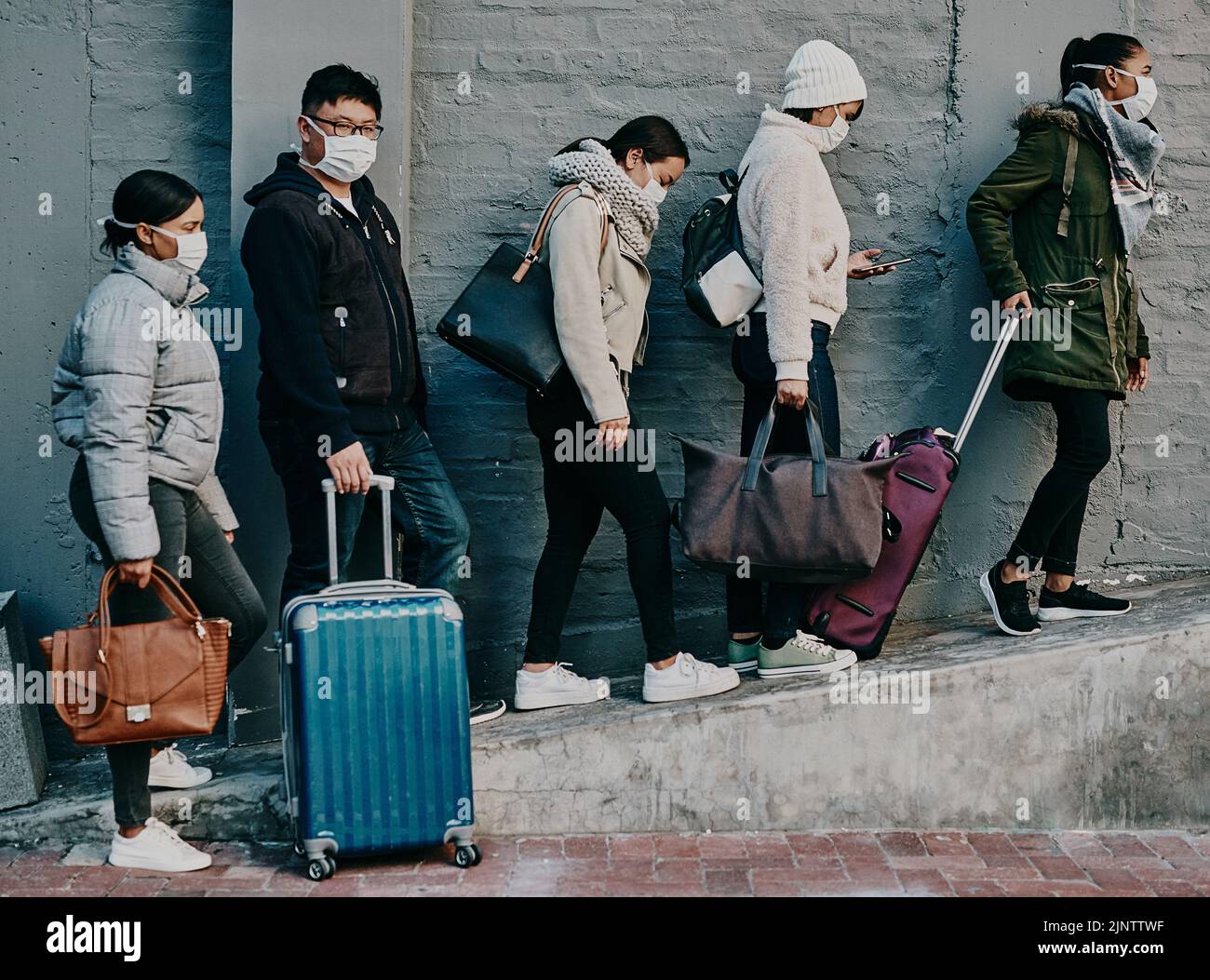 Traveling people wearing covid face mask and suitcases waiting in line