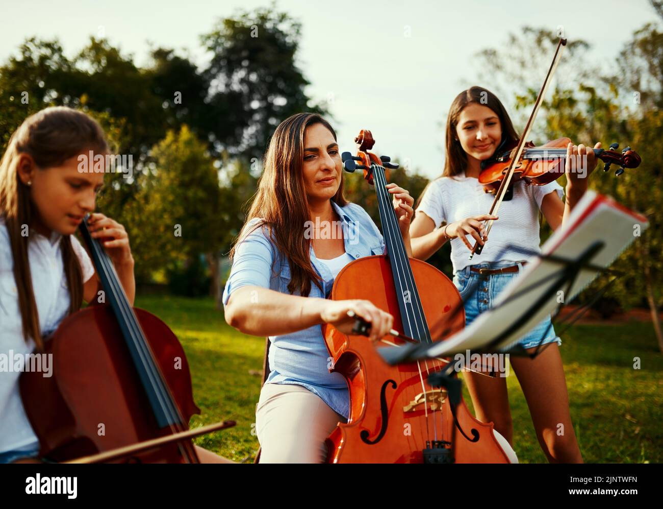 Being a band is great, being a family is better. a beautiful mother playing instruments with her adorable daughters outdoors. Stock Photo