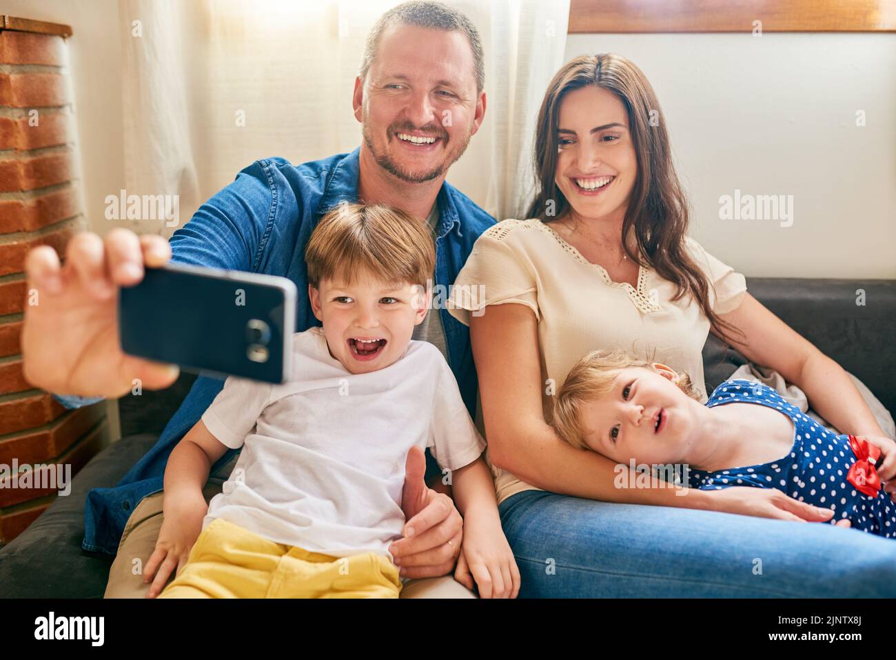 Make every family moment memorable. a happy young family taking a selfie together on the sofa at home. Stock Photo