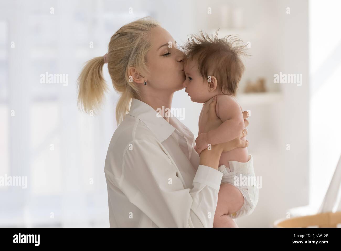 Young loving affectionate mother kisses newborn baby Stock Photo