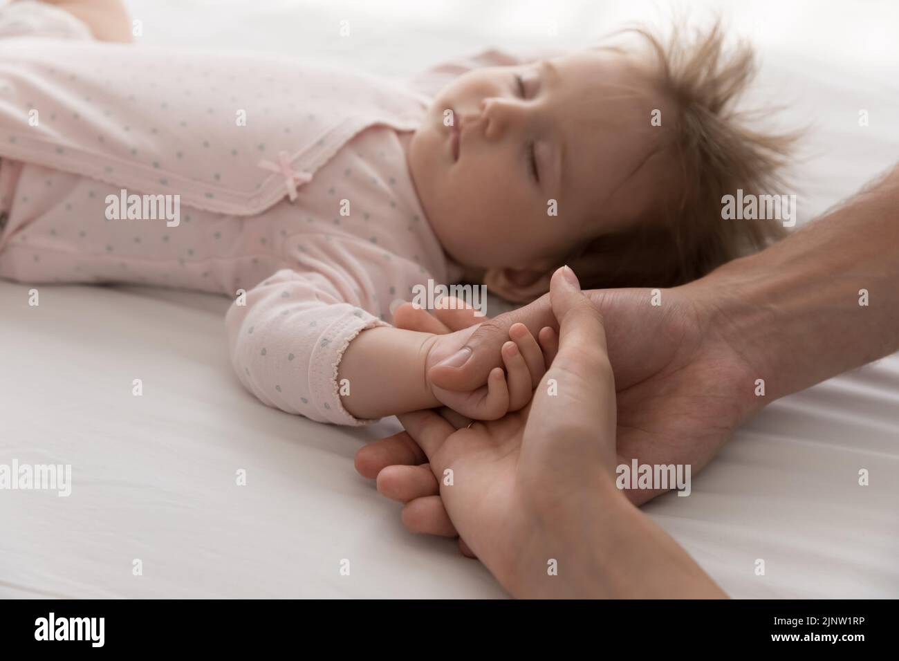 Loving parents touch tiny arm newborn sleeping baby, closeup shot Stock Photo