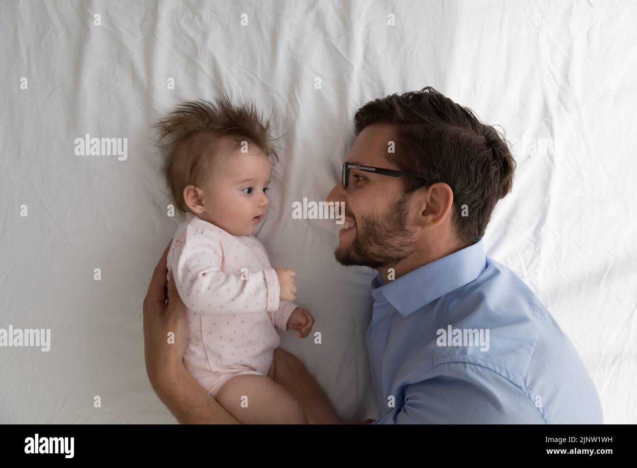 Loving father hugs baby lying together on white bedsheets Stock Photo