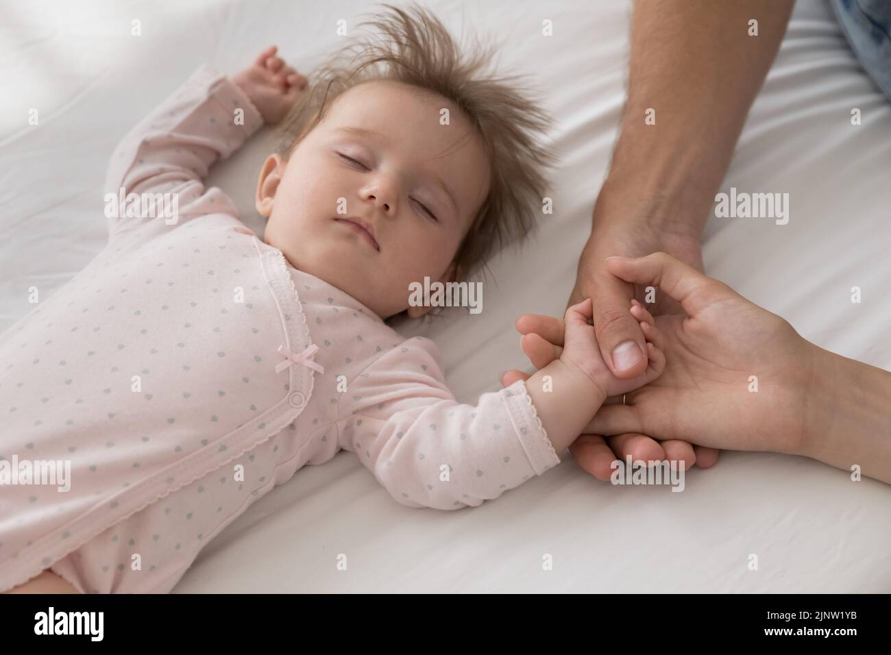 Cute newborn sleeping on bed touch loving parents hands Stock Photo