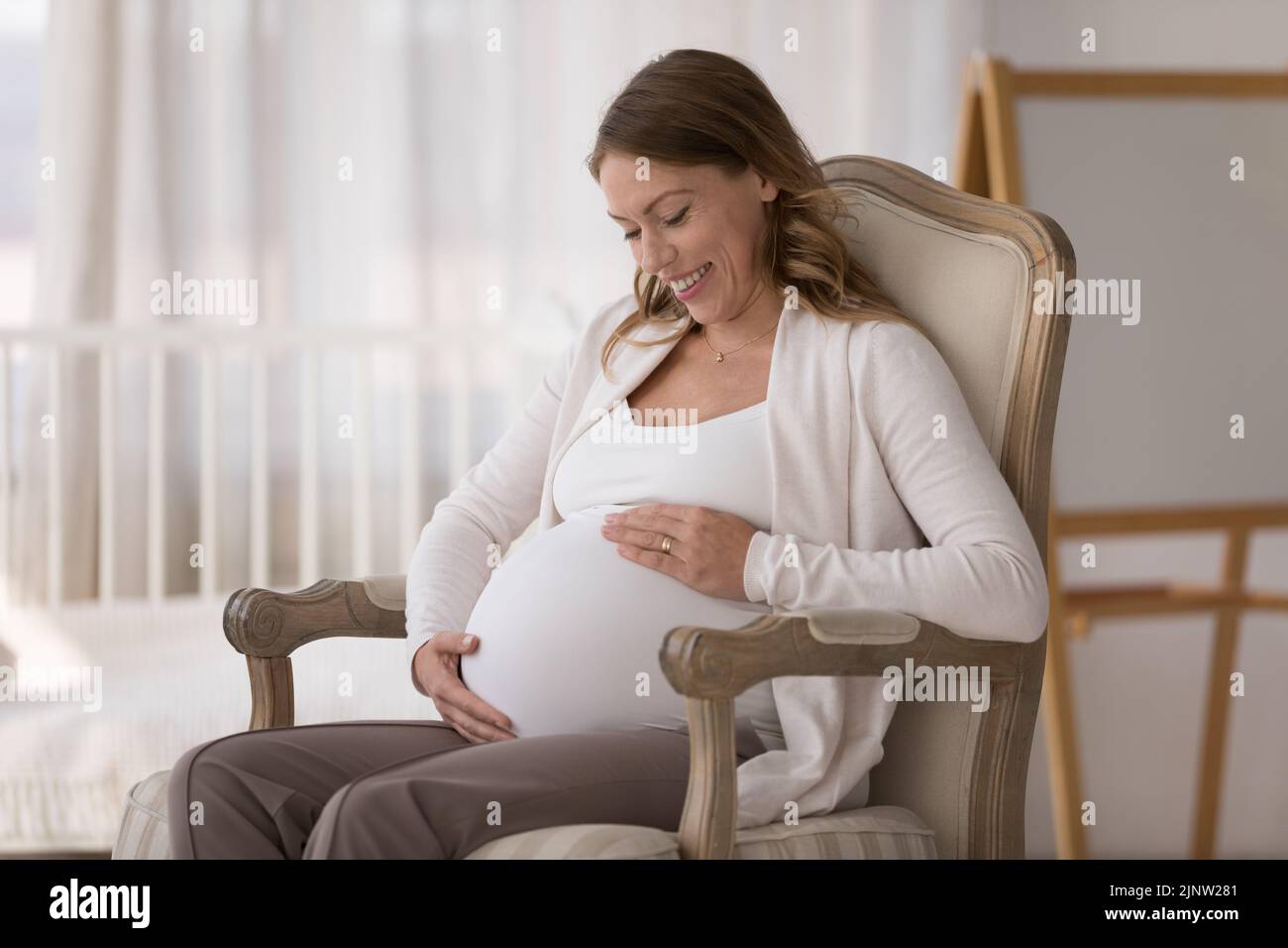 Young affectionate expectant mother relaxes in armchair at home Stock Photo