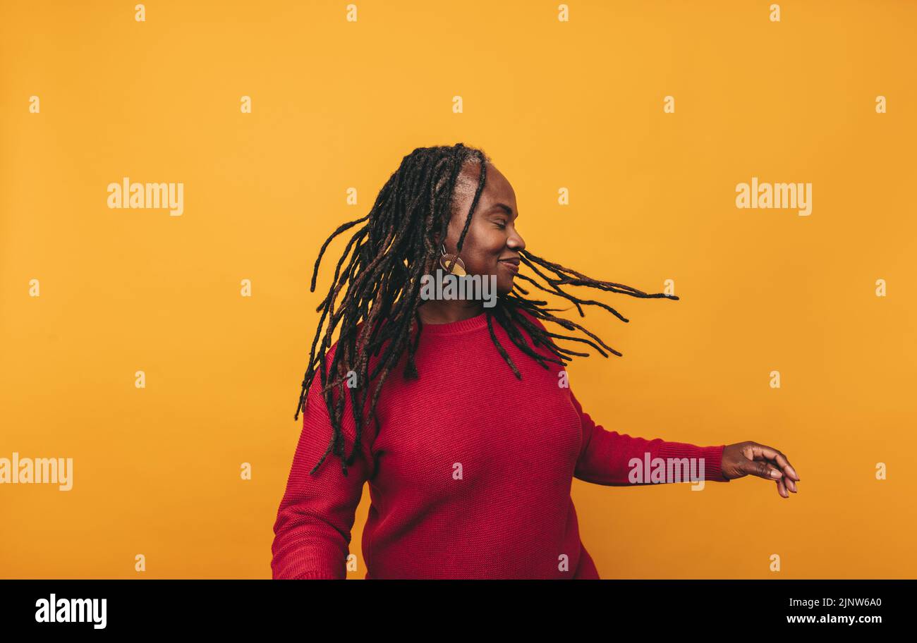 Joyful black woman dancing and whipping her dreadlocks while standing against a studio background. Happy middle-aged woman having fun and embracing he Stock Photo