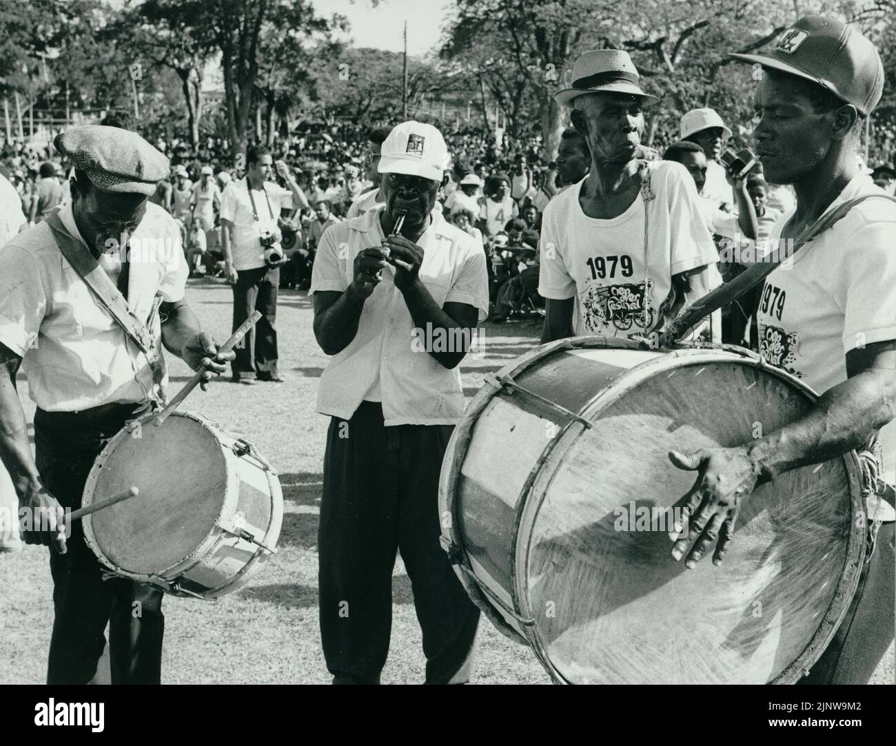 Black and white photograph of a Bajan band playing traditional folk music at a parade in Barbados, with a large crowd in the background Stock Photo