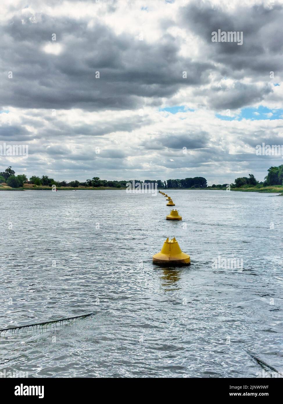 Row of yellow buoys in the Elbe river, marking a submerged steel cable. Stock Photo