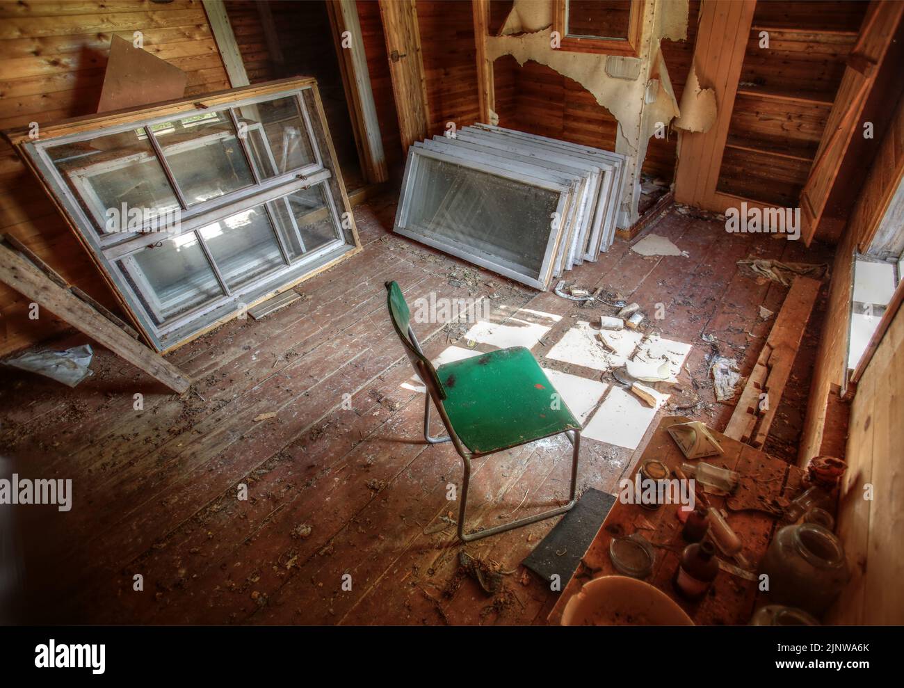 Ruined interior of an old wooden house with chair and disused windows. Stock Photo
