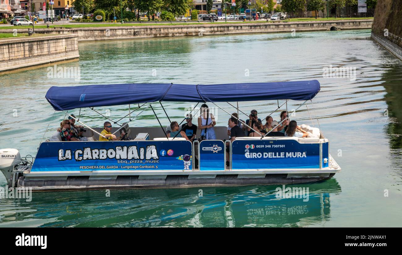 Boat with tourists and tour of the fortress walls of the town of Peschiera del Garda , Verona province, northern Italy. tourists on boat Stock Photo
